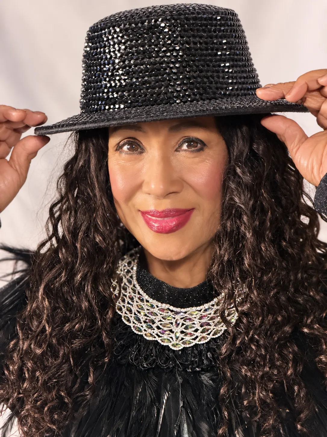 Kristina Mercado smiling at the DJ decks in her black fedora, headphones to one ear